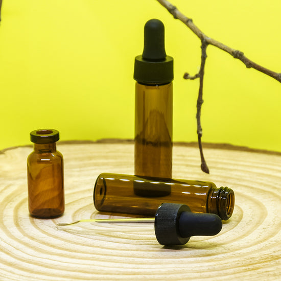amber glass dropper vials on top on brown wood platform with branch and yellow background