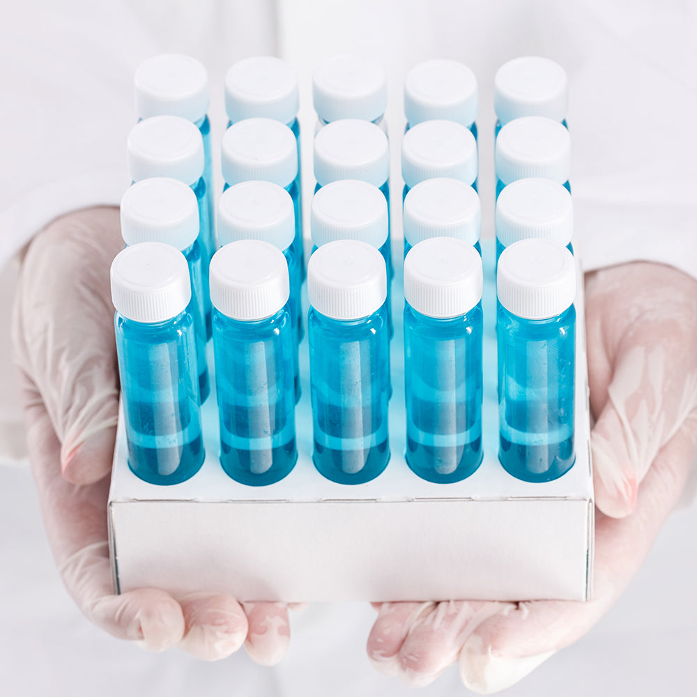scientist with clear plastic gloves holding clear EPA scintillations glass vials with blue liquid